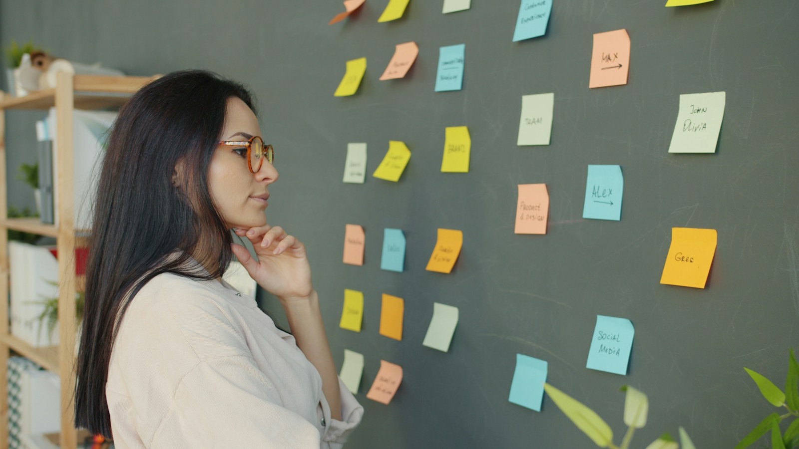 Mujer frente a una pared llena de notas adhesivas, pensando en sus ideas
